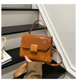 Detail view of brown crocodile texture flap and crossbody strap held by a hand - Brown