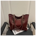 Primer plano de un bolso tote de charol burdeos con logo dorado sobre una silla negra - Rojo