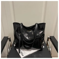 Detalle de bolso tote de charol negro brillante con logotipo sobre una silla negra - Negro