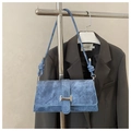 Close-up of blue denim baguette bag featuring silver buckles and knotted shoulder strap - Blue