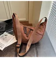 Detailed close-up of brown crescent crossbody bag with braided zipper and logo tag - Brown