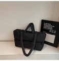 Macro detail of black quilted puffer tote bag with dual straps and soft padded texture - Black