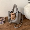 Grey litchi grain bucket bag with a plush dog charm on a rustic wooden stand - With Charm / Gray