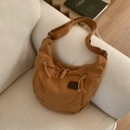 Detail of caramel canvas crescent shoulder bag with functional zippers on a sofa - Brown