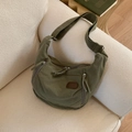 Olivgrüne Canvas-Halbmondtasche mit Reißverschlusstaschen auf einem gemütlichen Sofa - Grün