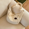 Detail einer beigen Canvas-Hobo-Tasche mit Reißverschlüssen und breitem Gurt auf Sofa - Weiß