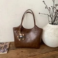 Detalle de bolso tote de cuero marrón oscuro con logo grabado y un colgante de peluche - Con Colgante / Marrón