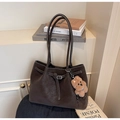 Detail view of large brown tote bag with leather texture, buckle strap, and plush bear charm - With Charm / Coffee