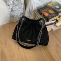 Detailansicht der schwarzen gesteppten Beuteltasche mit Kettenriemen und Logo auf Holzboden - Schwarz