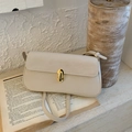 Detailed close-up of cream leather shoulder bag with golden U-shaped buckle on vintage books - White