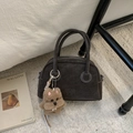 Makro-Detail der dunkelbraunen matten Ledertasche mit Nähten und Hundeplüsch-Anhänger - Braun