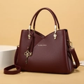 Close-up of wine red lychee leather texture and golden musical note key charms on handbag - Burgundy