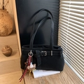 Detail of a black minimalist shoulder bag with buckle and plush bear charm on a wood table - With Charm / Black