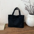 Bolso tote negro minimalista de ante con detalle de logo en superficie de madera rústica - Negro