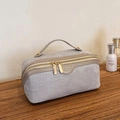 Neceser de gamuza gris con cremalleras doradas sobre una superficie de madera - Gris