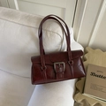 Retro weinrote Lederschultertasche mit Metallschnalle und dünnen Trägern auf weißem Sofa - Rot