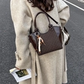Deep coffee bucket bag with checkered texture and beaded charm shown in a street view - Brown