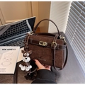 Detail of a brown leather crossbody bag with gold twist lock and dog charm on a desk - Coffee with Pendant