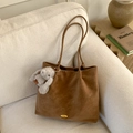 Detail view of brown vintage tote bag with gold hardware and plush rabbit charm on sofa - Brown (With Plush Charm)