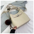 Close-up of cream leather handbag with silver turn-lock and brown fluffy pendant charm - Beige With Charm