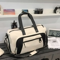 Large cream and black duffel bag with padded shoulder strap on a sleek black bench - White