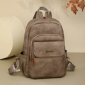 Detailed view of brown matte leather backpack with gold logo and front zipper pocket - Brown