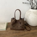 Detail einer Retro-Tweed-Tasche mit Tupfen und Lederbogen auf rustikalem Holz - Braun