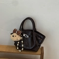 Détail d'un sac seau marron foncé brillant avec doubles poignées et breloque ours sur étagère - Avec Pendentif / café