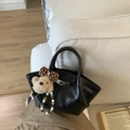 Glossy black bucket handbag with a plush bear charm on a cozy beige sofa - With Pendant / Black
