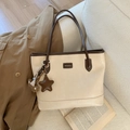 Detail of cream and brown contrast tote bag with star and bear charms on a sofa - Cream White With Pendant