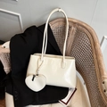 Beige oil-wax leather tote bag with heart charm hanging on a woven chair - White