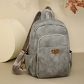 Detail of grey faux leather backpack featuring bronze twist lock and front zipper pocket - Gray