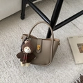 Detail of taupe lychee leather bucket bag with a cute bear charm on a plush white rug - With Pendant / Khaki