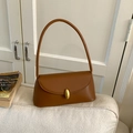 Detail of caramel leather shoulder bag with gold oval buckle on a white sofa - Brown