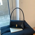 Detail of minimalist black leather underarm bag with gold oval clasp and cylindrical strap - Black