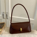 Dark brown leather baguette bag with oval gold buckle shown on a beige sofa - Brown