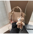Detail der beigen eckigen Handtasche mit Markenprägung und süßem Teddybär-Anhänger - Mit Anhänger / Aprikose