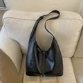 Close-up of black leather tote bag with silver buckle detail on a white sofa - Black