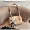 Detail of light brown glossy shoulder bag featuring bow ribbon and beaded charm on a sofa - With Charm / Khaki