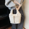 Light beige quilted tote bag with dual front pockets held by model in casual home setting - Off-white