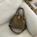 Detail of dark brown lychee leather bucket bag with gold twist lock and woven shoulder strap - Brown
