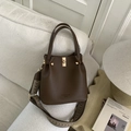 Detail of brown litchi leather bucket bag with wide geometric strap on sofa - Coffee