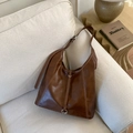 Détail du sac cabas marron avec surpiqûres contrastées et anneau argenté sur un canapé - Marron
