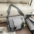 Deep grey waterproof nylon messenger bag with green dinosaur plush on beige sofa - With Charm / Gray