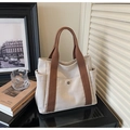 Close-up of canvas tote bag showing side pockets and brown handles on a modern desk - Off White
