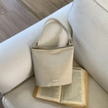 Chic cream-colored leather shoulder bag with gold buckles on a white sofa backdrop - Milk White