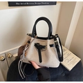 Detail of beige woven bucket bag with black leather straps and heart charm in a chic room - With Charm / Black