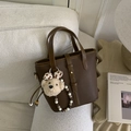 Sac seau marron foncé en cuir grainé avec charme d'ours sur un canapé en polaire - Marron avec pendentif