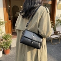 Classic black leather crossbody bag with silver buckle worn by a model in outdoor setting - Black