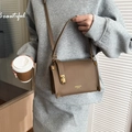 Brown lychee leather shoulder bag with gold twist-lock worn by model in a modern room - Elephant Gray